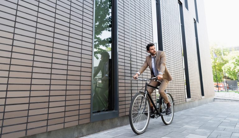 full length of businessman in suit riding bicycle and looking away near building