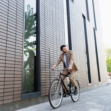 full length of businessman in suit riding bicycle and looking away near building